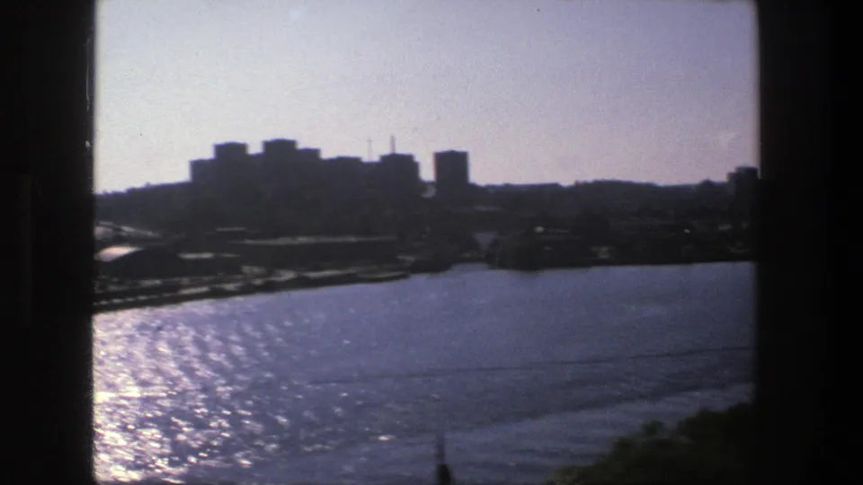 1975 Stockholm waterfront seen from above, with shimmering blue water and dark city buildings along the far shore.