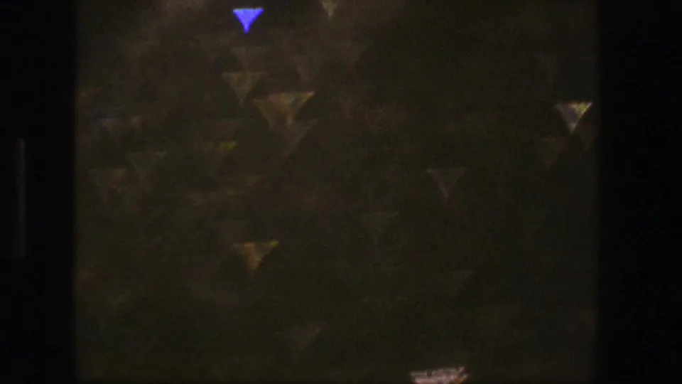 End-of-clip 8mm film texture with dark grain, soft color cast, and small triangular light flares.