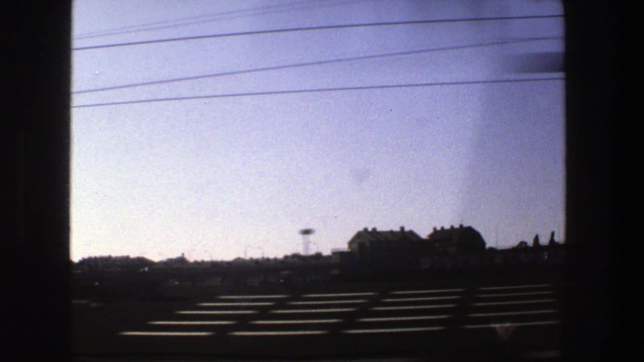 Silhouetted roadside buildings and landscape beneath a pale sky crossed by power lines.