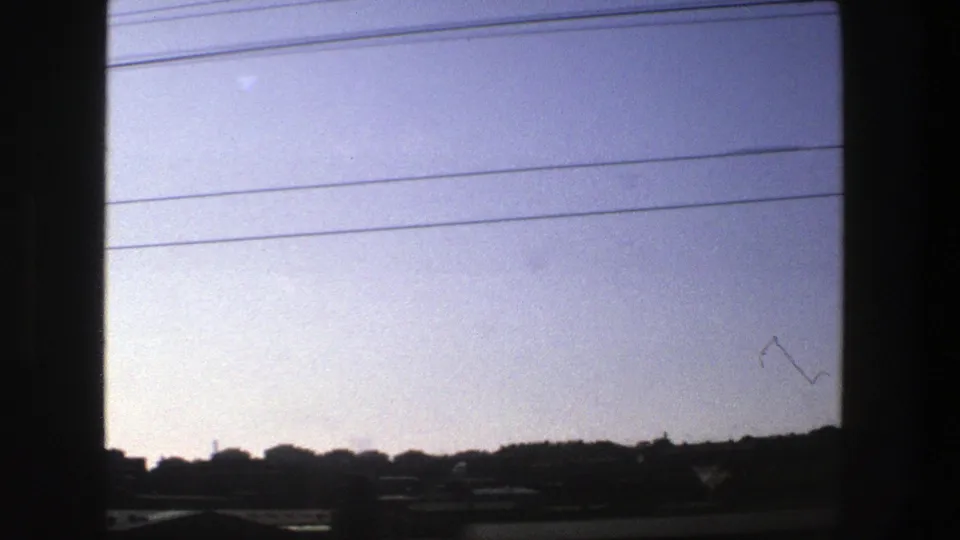 Late-frame 1975 Stockholm travel view through a vehicle window, with pale sky, power lines, low horizon, and roadside elements.