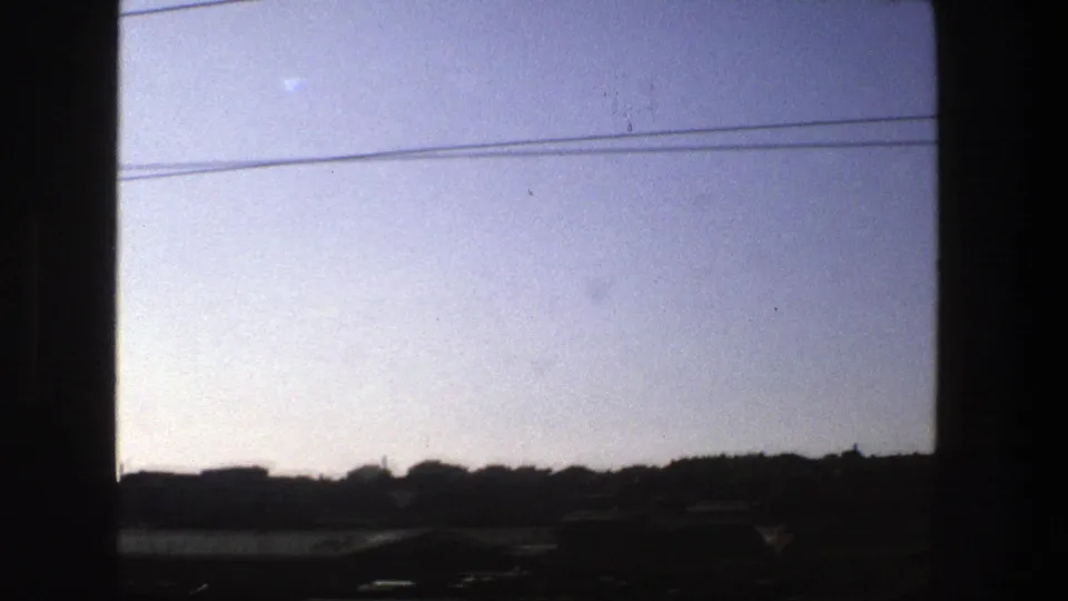 1975 Stockholm train-window view with dark frame edges, overhead cables, and a silhouetted urban skyline under a hazy sky.