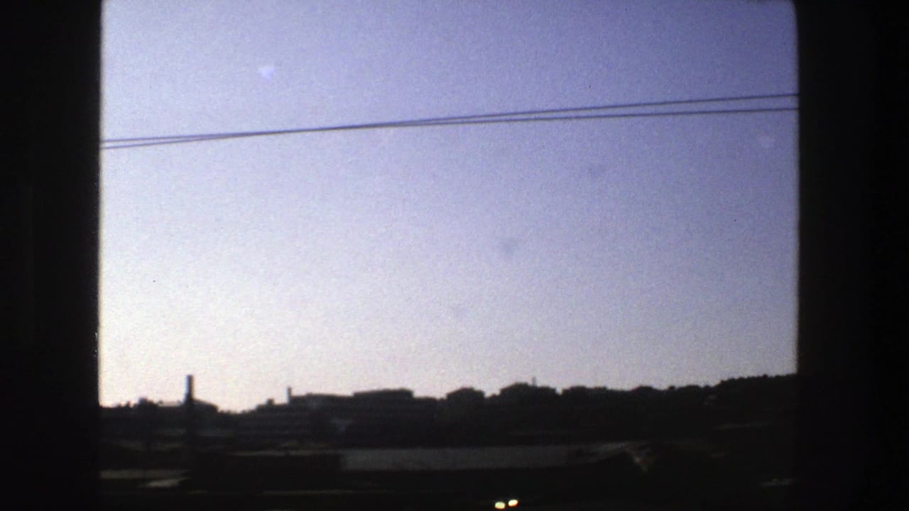 Stockholm rail-side city view from 1975, with two overhead cables stretching across a hazy sky above silhouetted buildings.