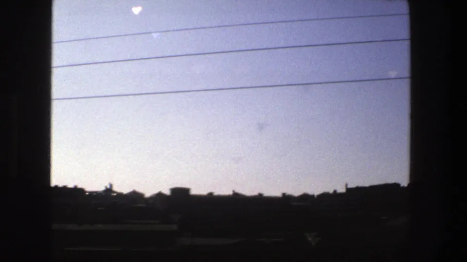 Stockholm in 1975 appears as a silhouetted rail-side cityscape below overhead cables, with 8mm grain and window framing.