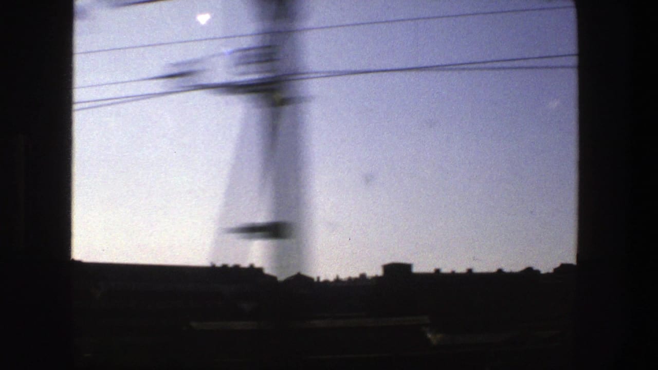 Dark train-window view of a skyline, overhead wires, and clear sky.