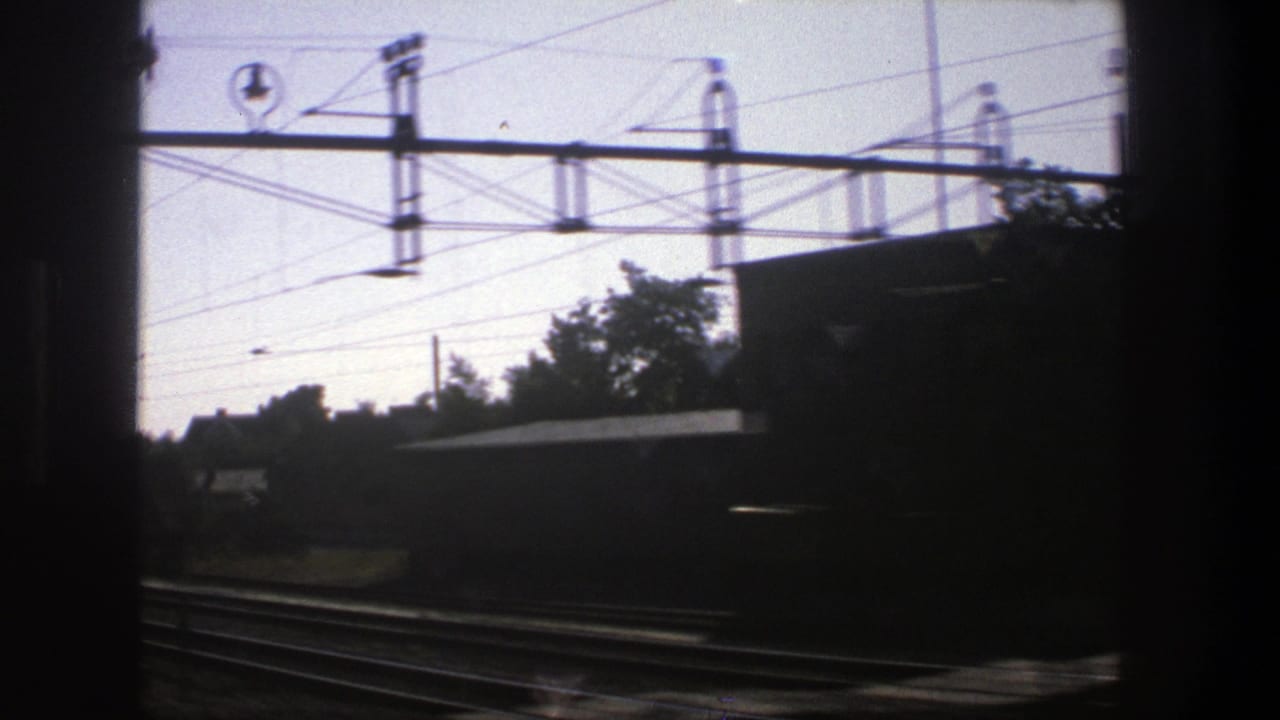 Railway tracks and overhead electric lines seen from a moving train window.