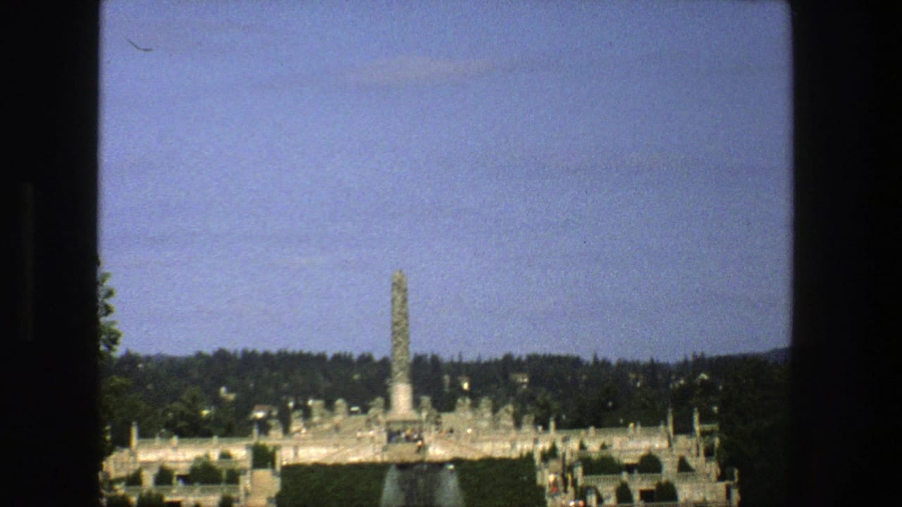 Stockholm landmark view on 8mm film, framed by window edges with a tall monument, park paths, trees, and small visitors.