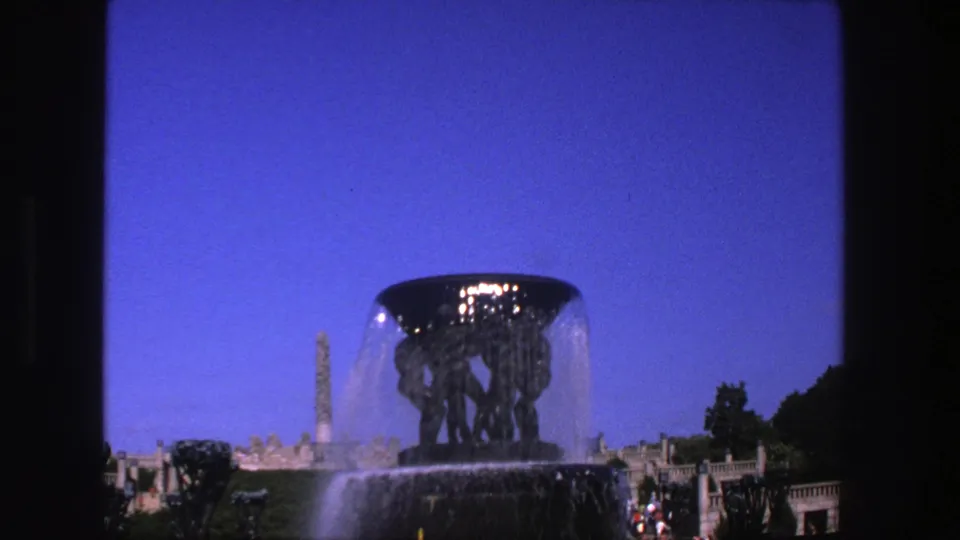 1975 8mm travel frame identified as Stockholm, showing a closer fountain view with falling water, blue sky, trees, and distant visitors.