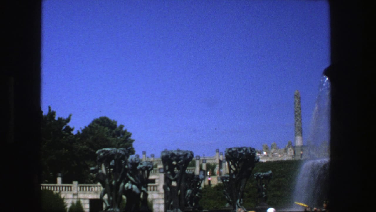 1975 Stockholm 8mm frame showing bronze fountain figures, cascading water, park terrace, greenery, and a distant obelisk-like monument.