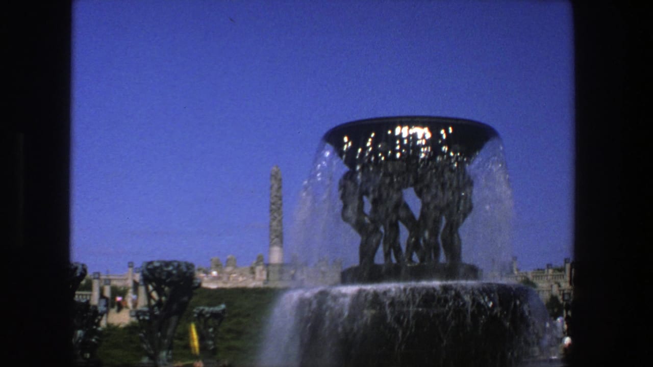 1975 Stockholm 8mm frame showing a public fountain sculpture with falling water, the obelisk in the background, and distant park visitors.