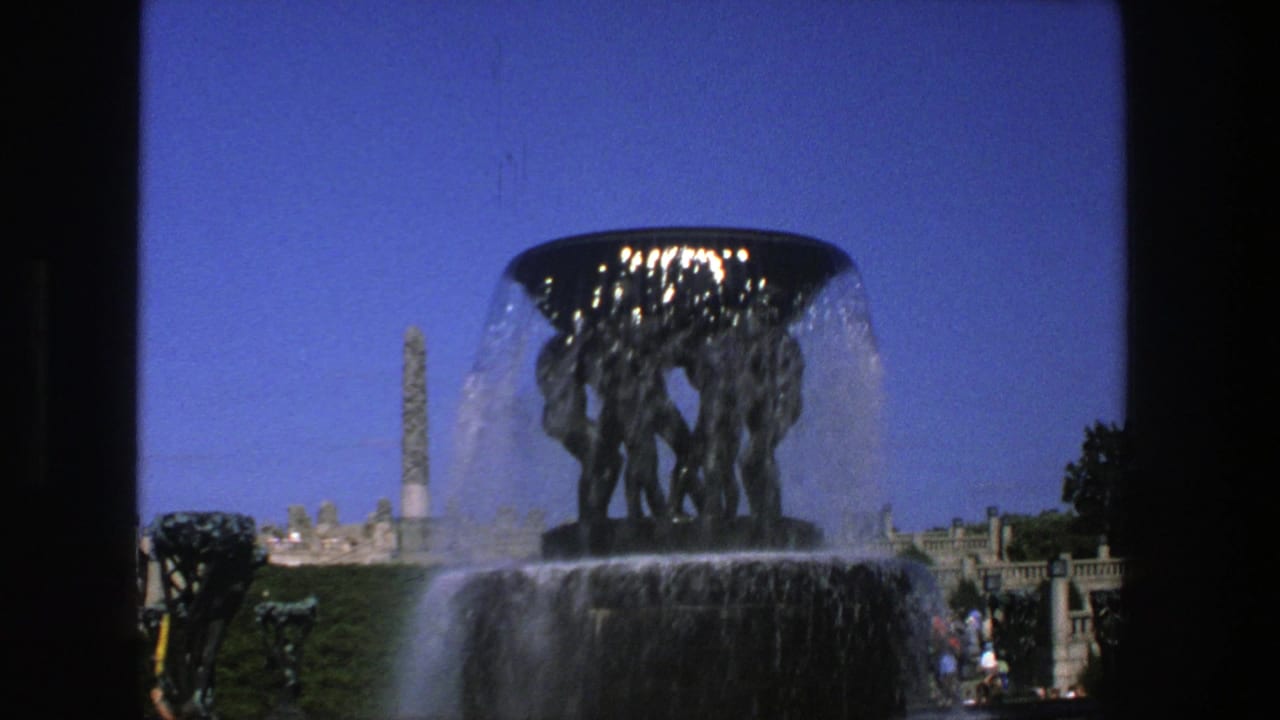 Centered fountain with water spilling over sculpture, obelisk at left, and small figures in the distance.