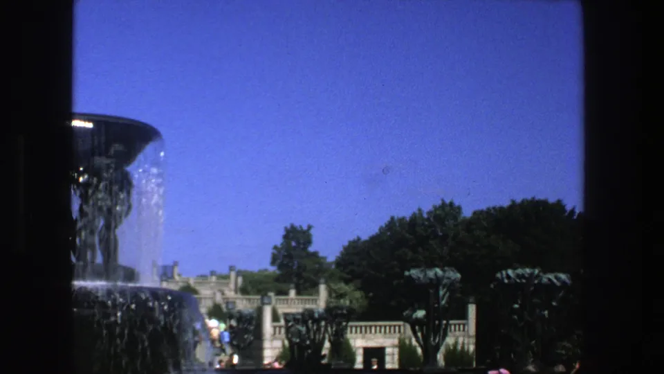1975 Stockholm 8mm frame with the fountain partly cropped at left, trees and stone park architecture across the background.
