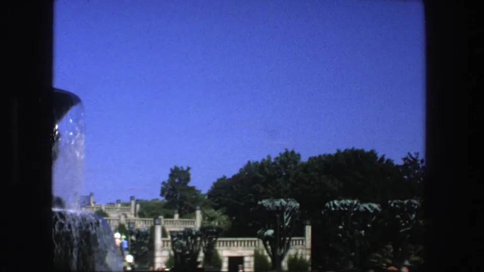 Final 1975 Stockholm frame showing the fountain at the left edge with trees, stone park structures, and distant visitors.