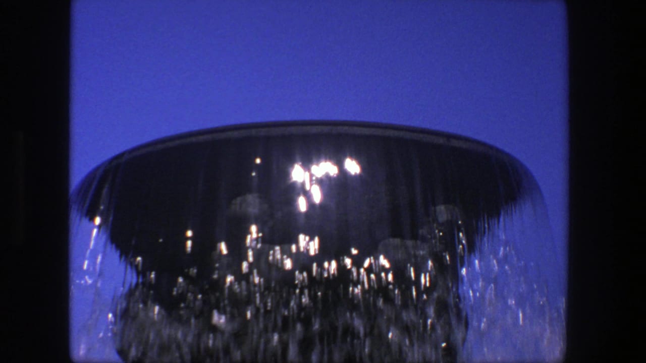 Close view of water cascading over the rim of a dark stone fountain bowl.