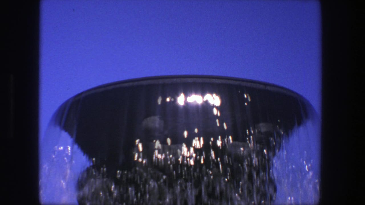 Circular fountain rim with cascading water against a deep blue sky.