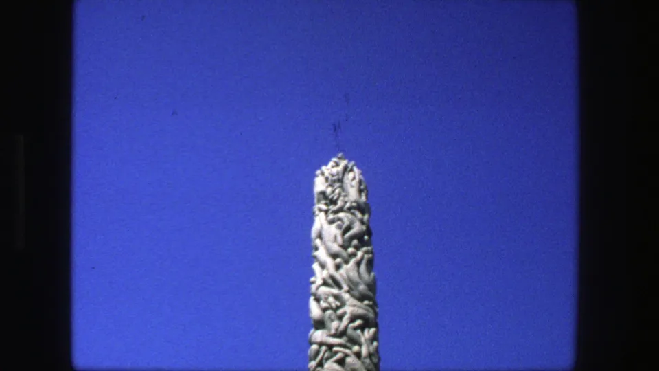 1975 Stockholm 8mm frame showing a carved vertical stone monument from a low visitor angle against saturated blue sky.