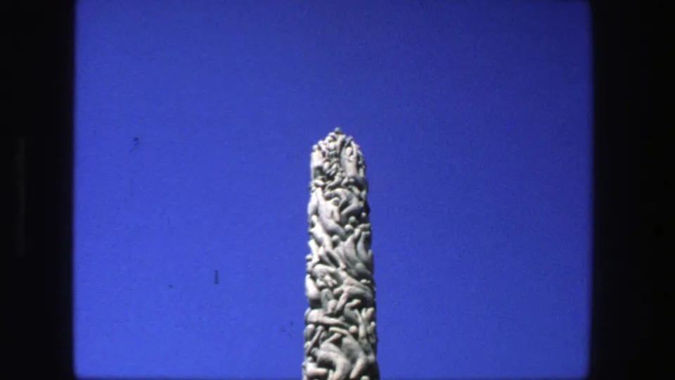1975 Stockholm 8mm frame of a tall carved stone obelisk centered in a simple blue-sky composition.