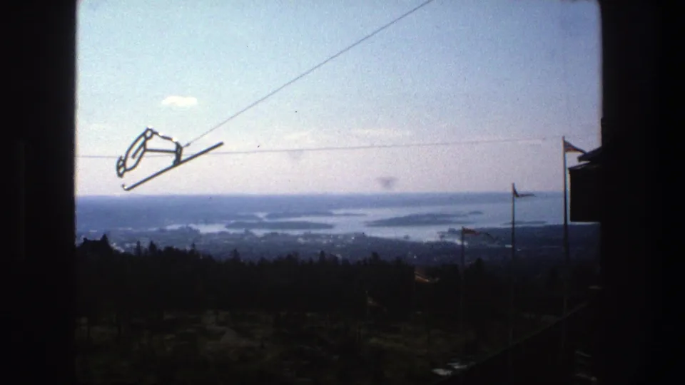 Elevated 1975 Stockholm view with suspended cable hardware, dark foreground framing, trees below, and hazy water and islands beyond.