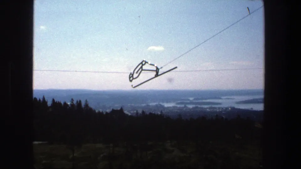 1975 Stockholm home-movie still showing a cable car line above dark trees and distant archipelago waterways.