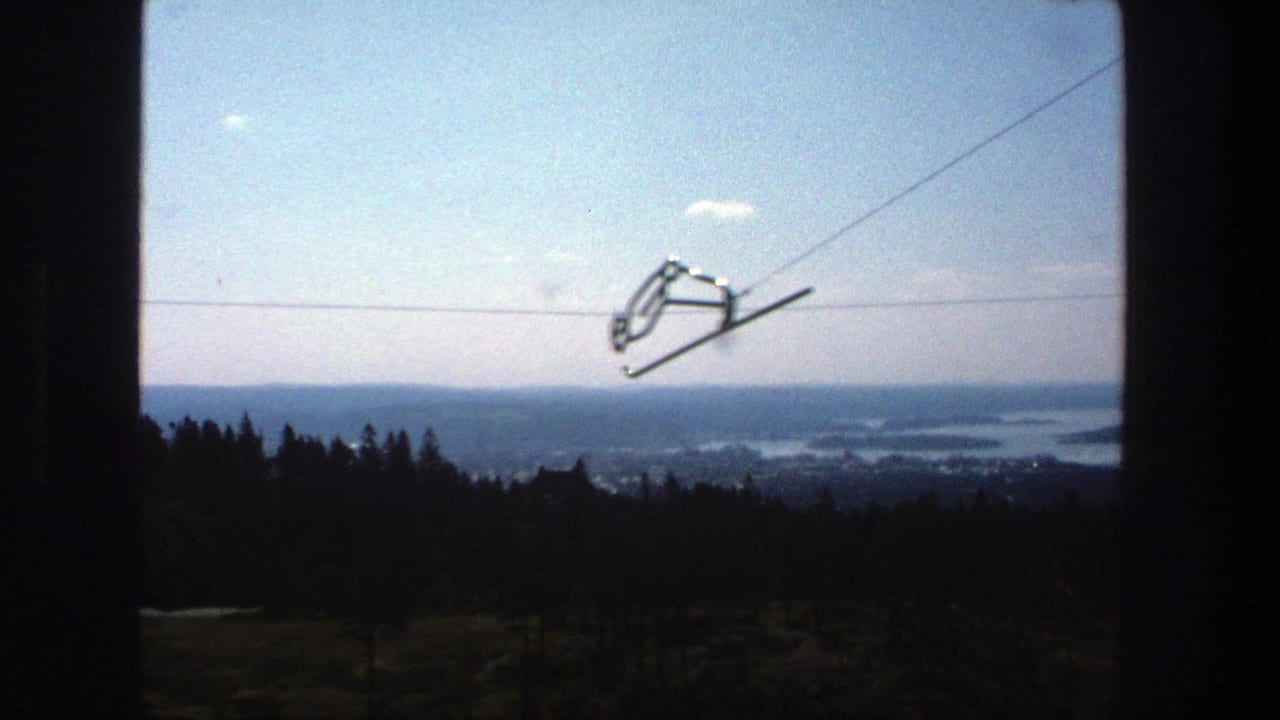 Ski-lift chair silhouetted on a cable above a distant wooded city and water view.