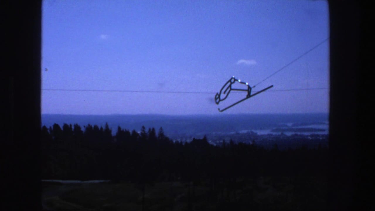 Ski-lift chair on cables crossing a blue sky above a dark tree line and distant water.