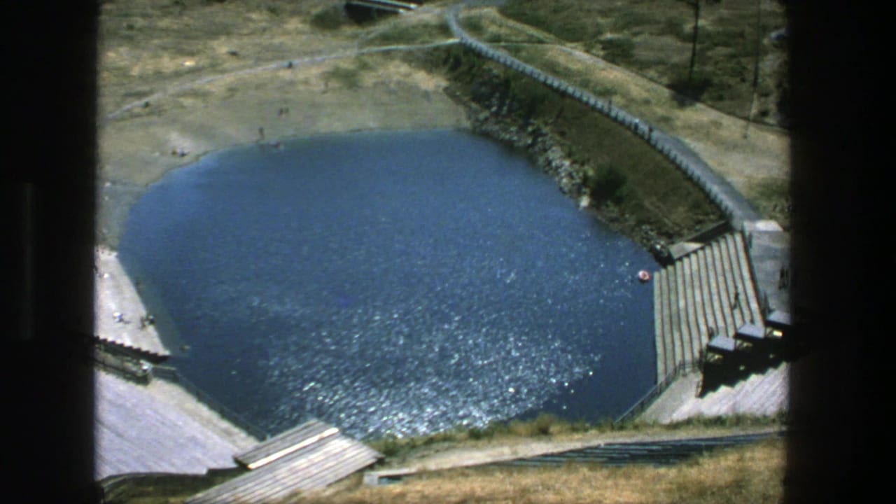 Outdoor pool seen from above with sparkling water, concrete steps, paths, and a red ring near the edge.