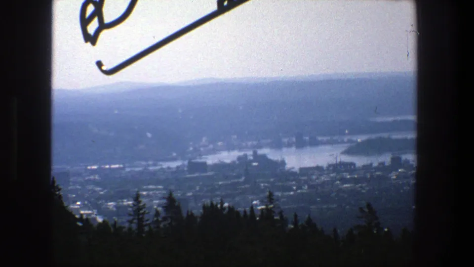 1975 Stockholm frame showing a hazy distant city and waterways through a dark window frame, with a silhouette of trees below.