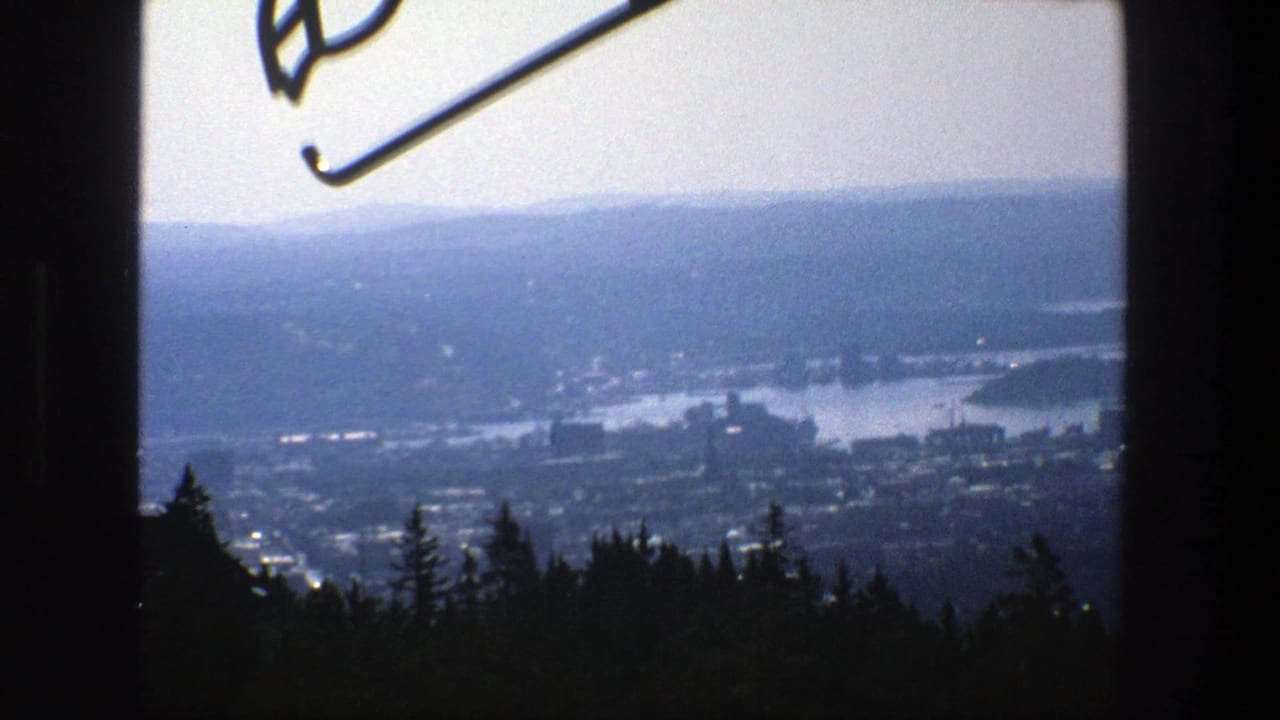 1975 Stockholm cityscape seen from an elevated wooded viewpoint, with water, distant hills, and part of a ski-jump element at the top edge.