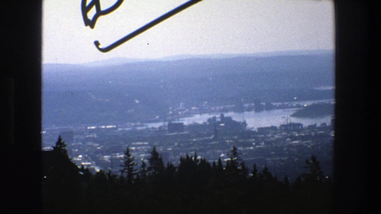 Elevated 1975 view across Stockholm with water, urban development, wooded foreground, and a partial ski-jump element near the upper edge.
