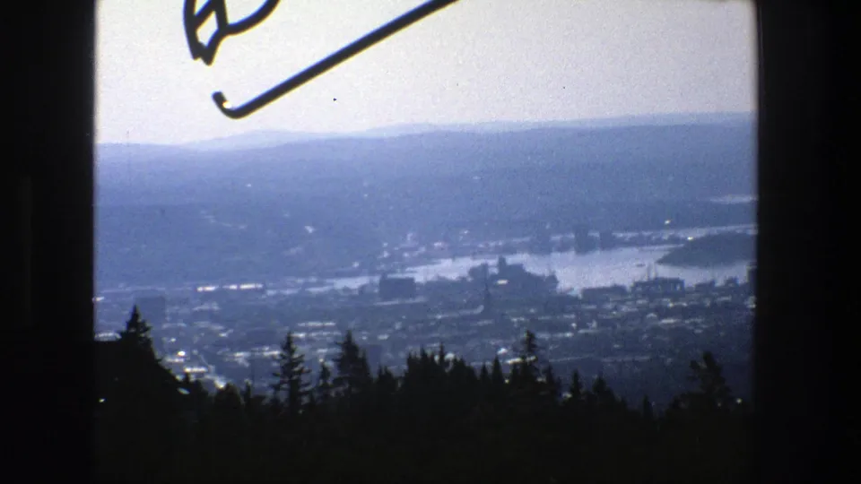 Elevated 1975 view across Stockholm with water, urban development, wooded foreground, and a partial ski-jump element near the upper edge.