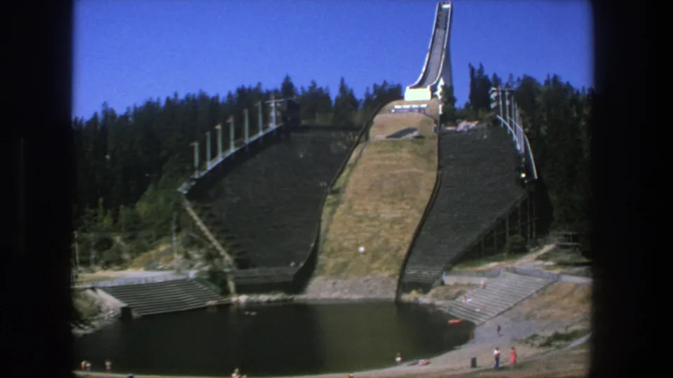 Final 8mm frame holds on the stated Stockholm ski jump scene, with water below and a few small visitors along the paths.