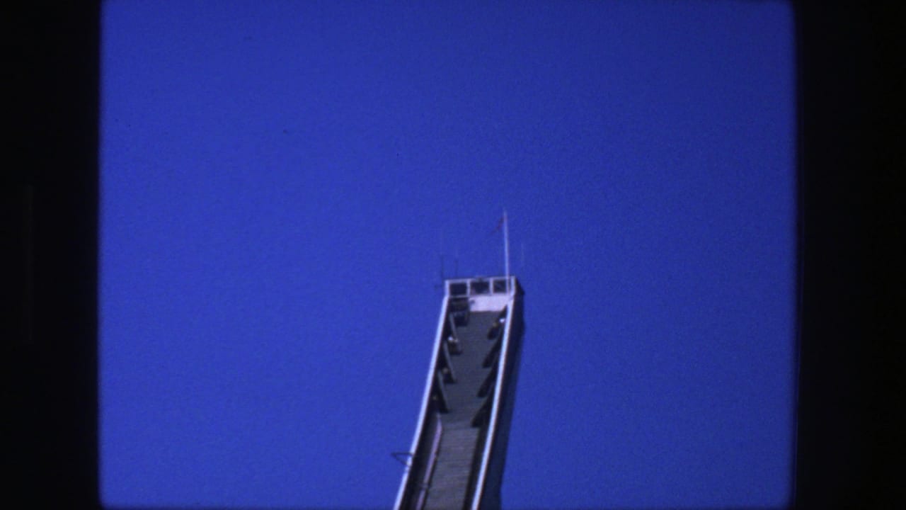 Top portion of a white ski jump ramp against a deep blue sky.