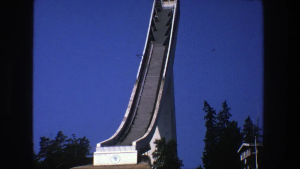 Fuller 1975 Stockholm view of the white ski jump ramp, its base, railings, and nearby trees in bright daylight.