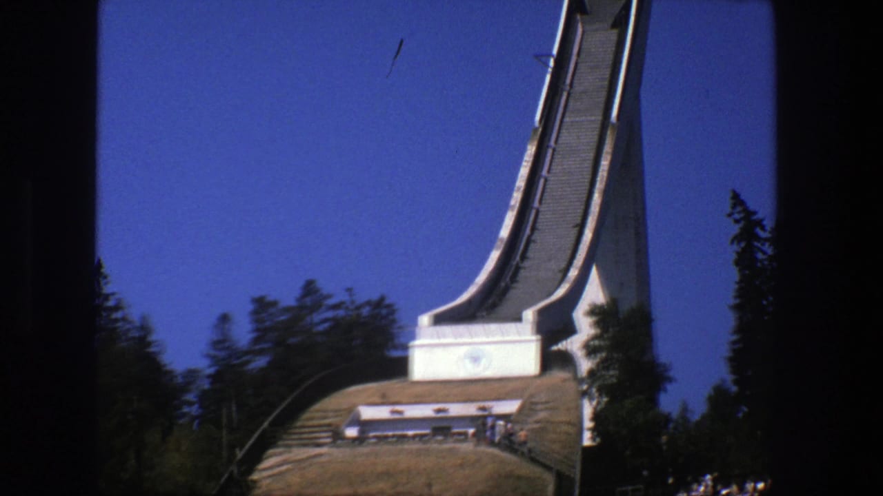 Ski jump tower base and lower slope with trees and distant spectators.