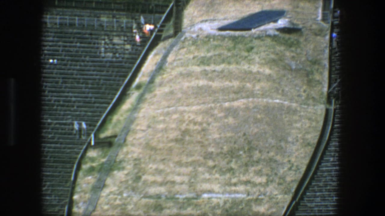 High-angle view of tan ground beside dark rows of seating and a sloped edge.
