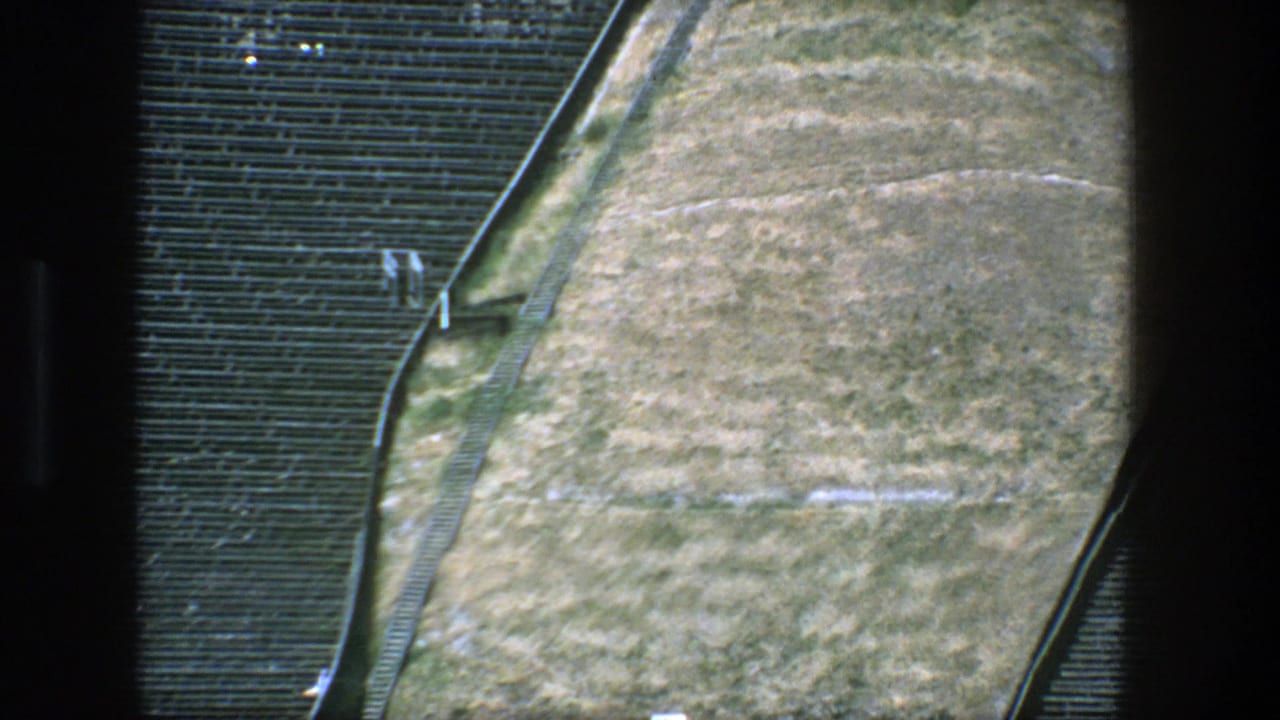 Tan sloped ground bordered by rows of seating and railings.