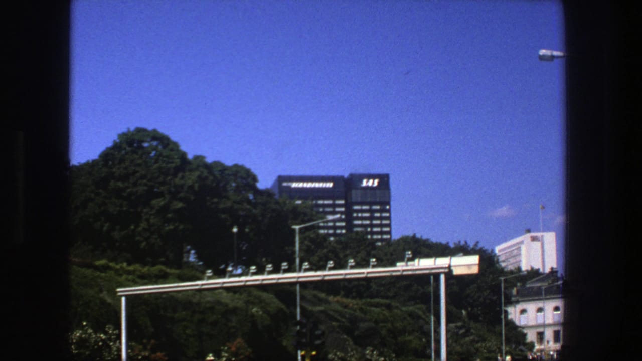 Stockholm urban landscape from 1975 showing green trees, a SAS-marked office building, streetlights, and clear blue sky.