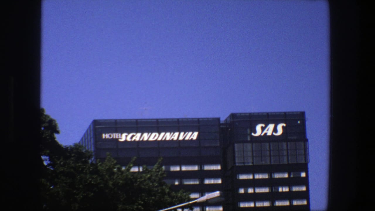 Hotel Scandinavia and SAS signs on a dark building above trees and a blue sky.