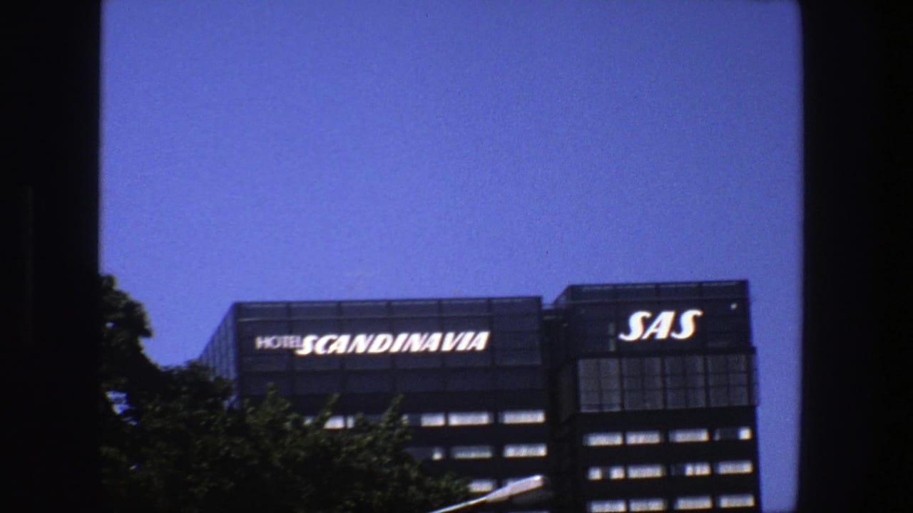 Street-level 8mm view in Stockholm with Hotel Scandinavia and SAS signage across the top of a dark building.