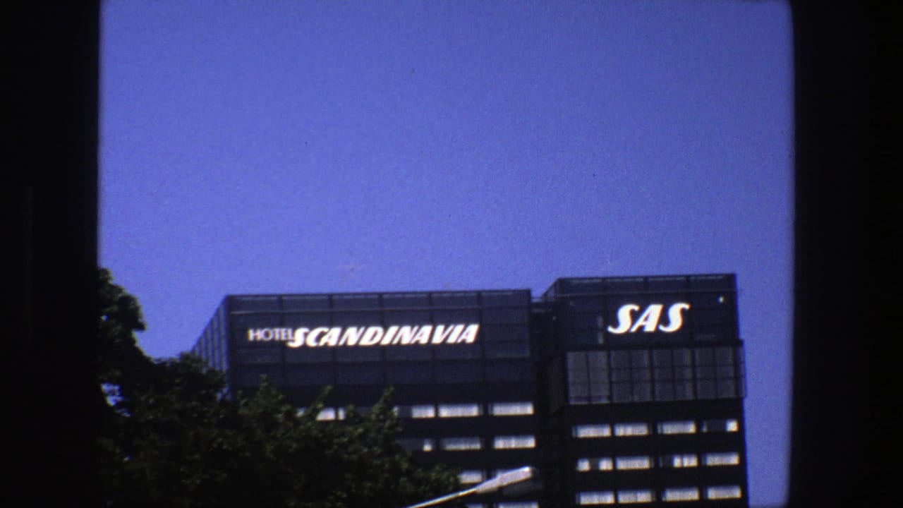 1975 Stockholm exterior frame with trees obscuring part of the Hotel Scandinavia and SAS building facade.