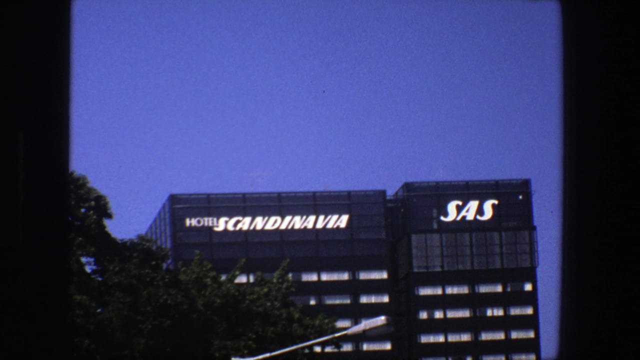 Final 8mm frame of the Stockholm building exterior with Hotel Scandinavia and SAS signs above a leafy foreground.