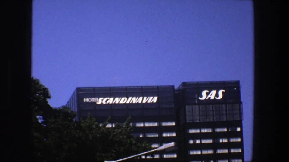 Final 8mm frame of the Stockholm building exterior with Hotel Scandinavia and SAS signs above a leafy foreground.