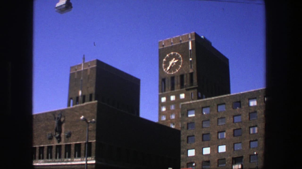 1975 Stockholm frame with a prominent clock tower, brick facades, and a clear blue sky in a handheld 8mm composition.