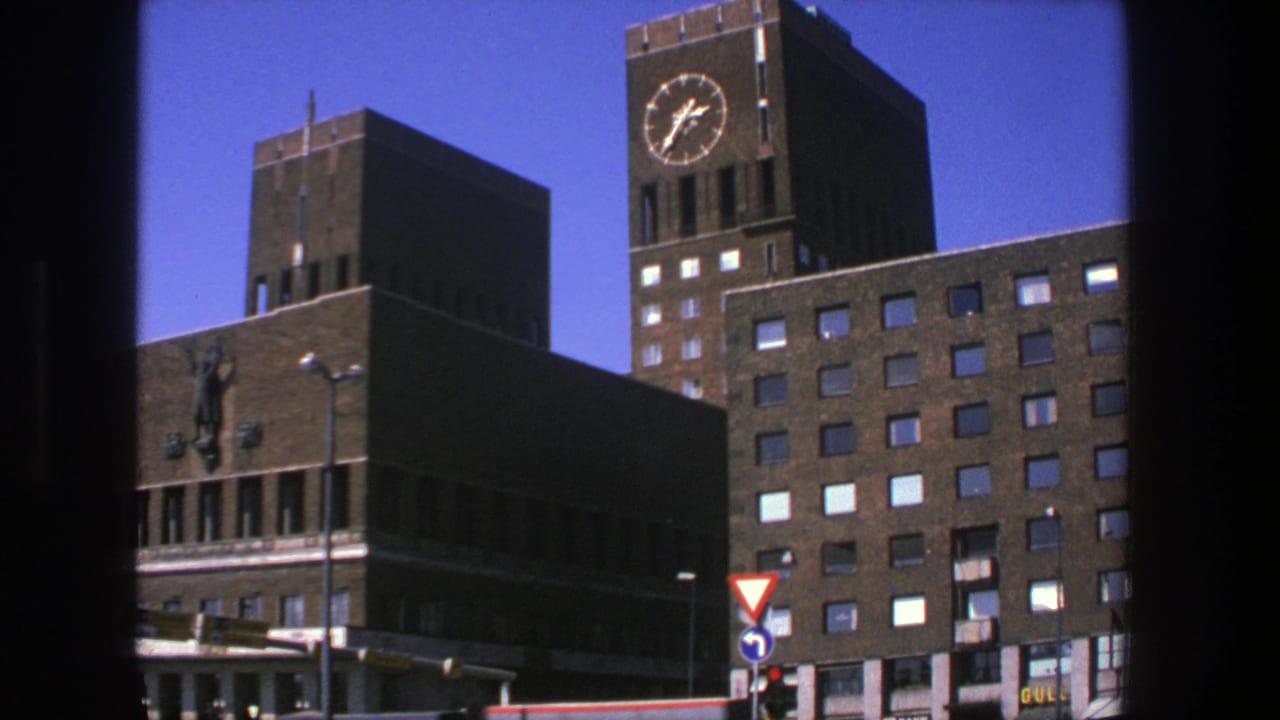 Brick clock tower and lower building seen across a street with traffic signs.
