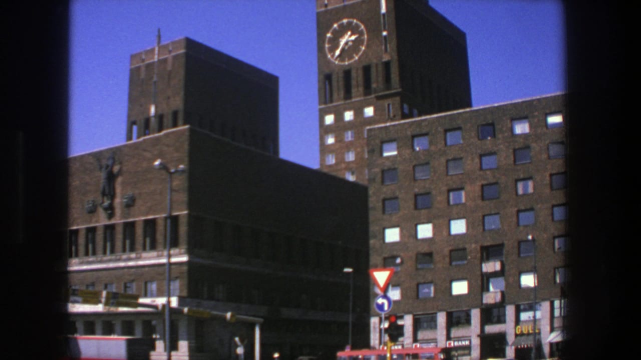 1975 Stockholm view of a brick clock-tower building with traffic signals, a yield sign, and small commercial signage at street level.
