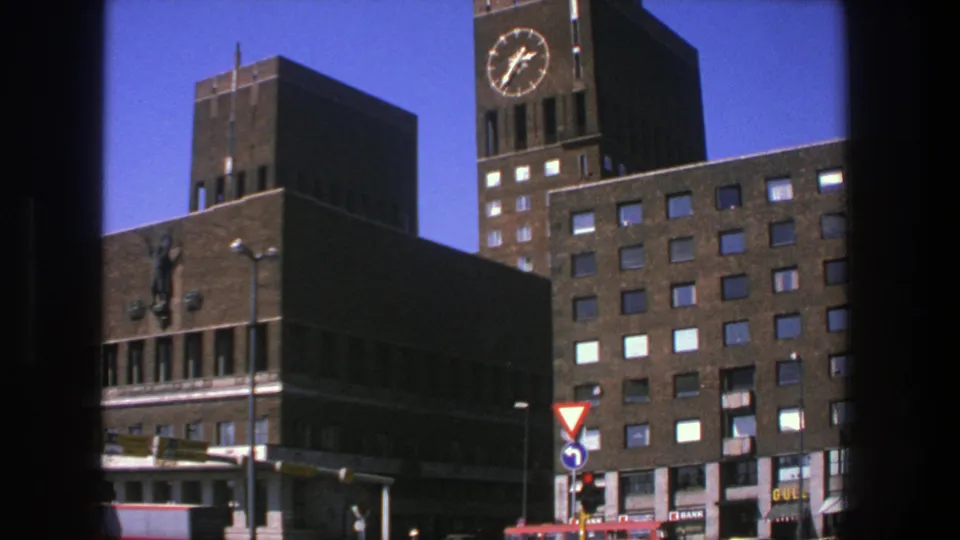 1975 Stockholm view of a brick clock-tower building with traffic signals, a yield sign, and small commercial signage at street level.