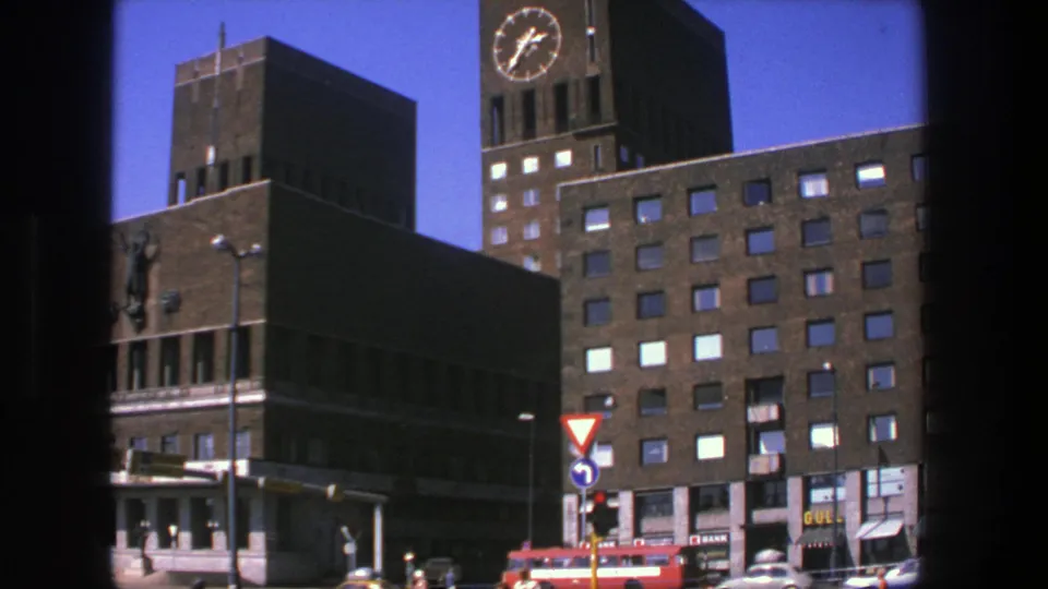 1975 Stockholm street view showing brick civic architecture, a clock tower, red bus, cars, and traffic signals from a window-framed angle.
