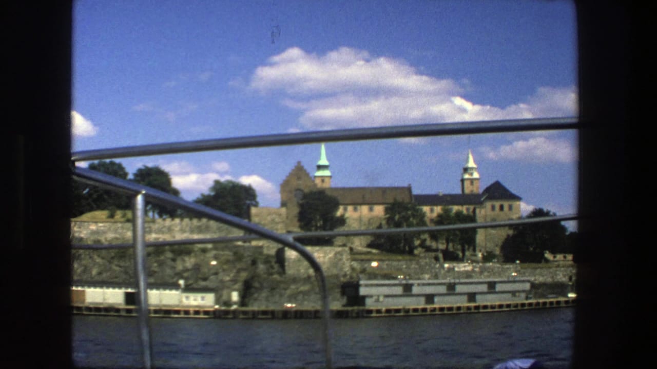Stockholm, Sweden in 1975, with a historic stone complex and towers viewed from a boat under a blue sky.
