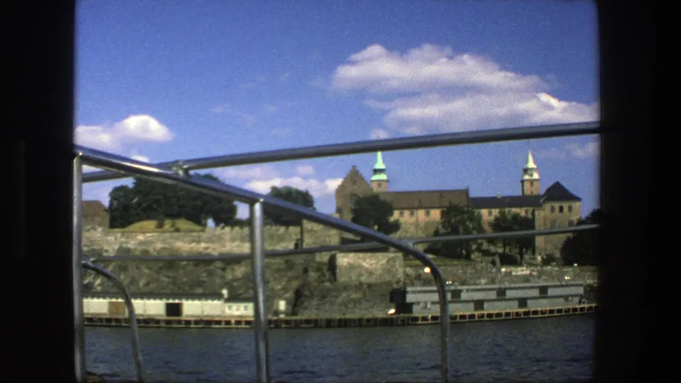 Stockholm waterfront architecture in 1975, filmed from a boat with railings, water, trees, stone walls, and towers in view.