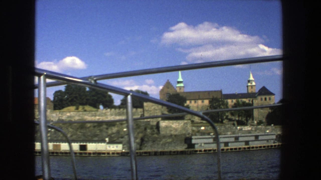 Boat railing frames a historic waterfront fortress across dark water under a blue sky.