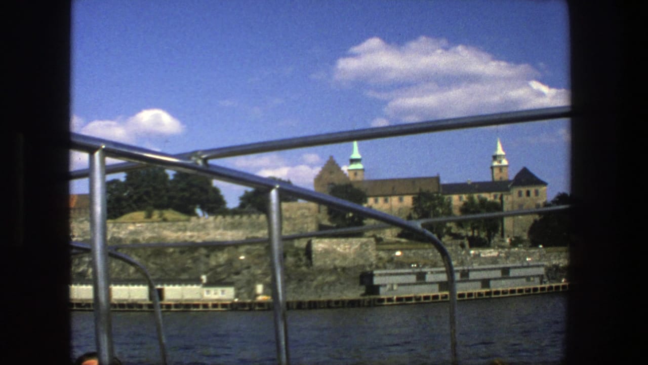 Stockholm waterfront architecture appears behind metal boat railings, with stone walls, trees, water, and bright clouds in a 1975 travel-film frame.